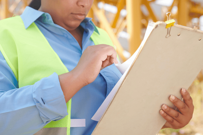 Worker in a safety vest reviewing an inspection checklist on a clipboard at a construction site.