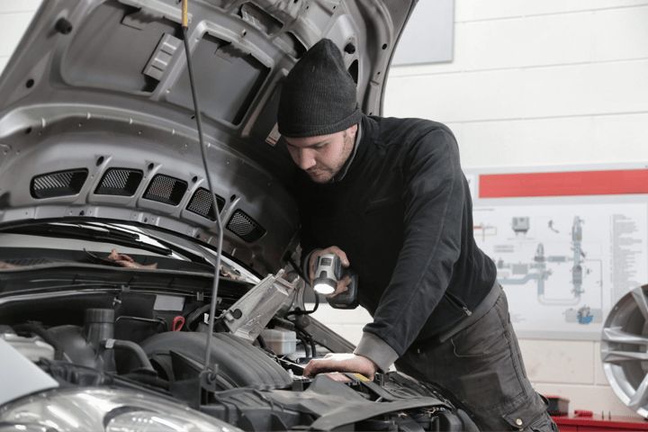 Mechanic using a flashlight to inspect under a vehicle hood during a fleet inspection.