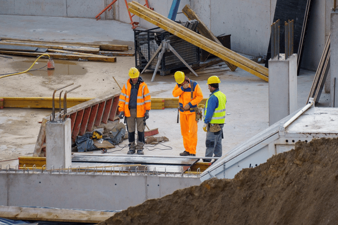 Three engineers in hard hats are discussing on a construction site.
