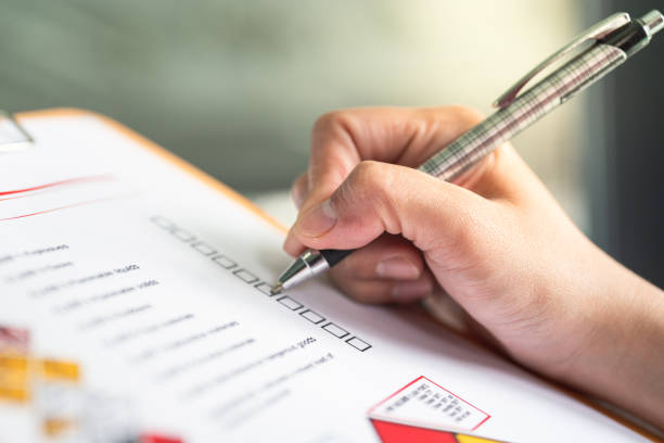 A close-up of a hand holding a pen, filling out a checklist form on paper.
