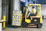 Worker in a high-visibility vest operating a yellow Hyster forklift carrying stacked cases in a warehouse