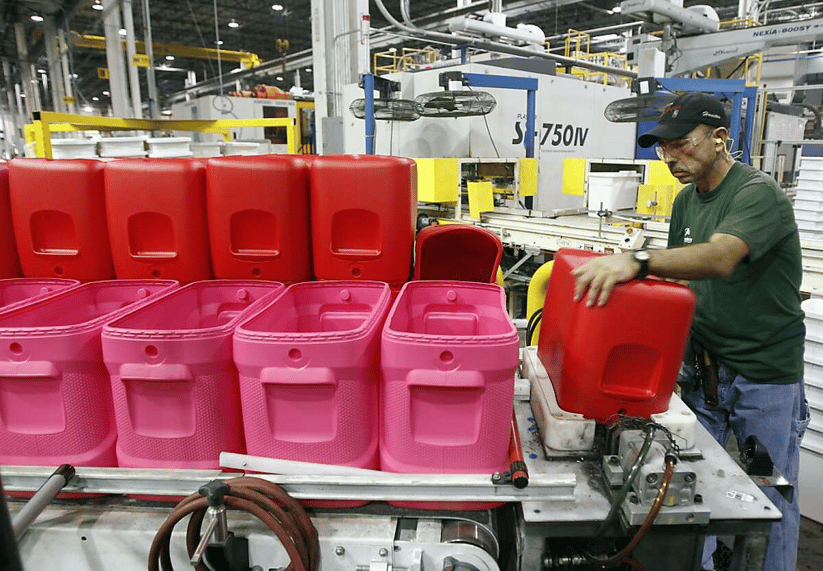 Factory worker handling red plastic containers on a production line in a manufacturing facility.