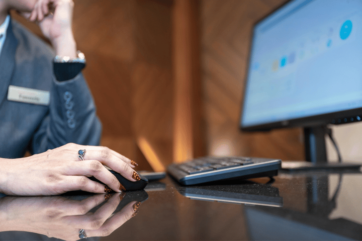 Close-up of a hand using a computer mouse on a glossy desk with a keyboard and monitor nearby.