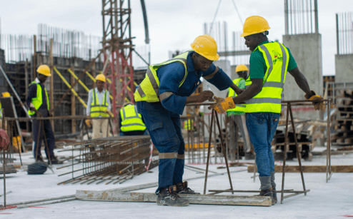 Construction workers in safety vests and helmets are inspecting a building site.