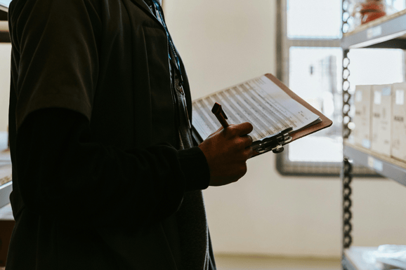 Person in dark clothing holding a clipboard with an audit checklist and pen while conducting an inspection.