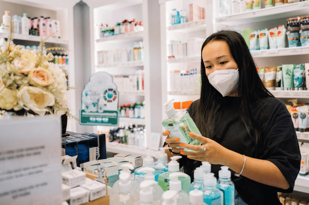 Woman wearing a face mask examining products at a counter in a pharmacy.