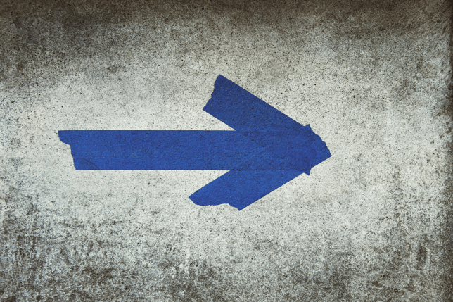 Blue arrow painted on a weathered concrete surface pointing to the right.