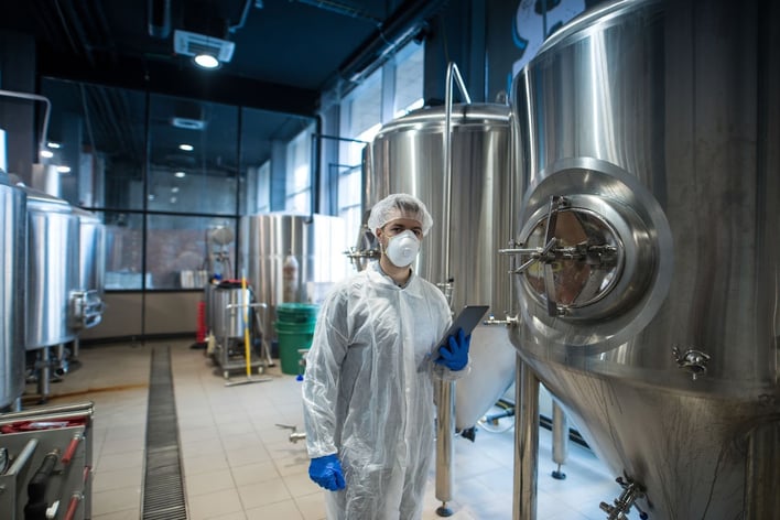 Technologist in a white protective uniform holding a tablet in a food processing facility.