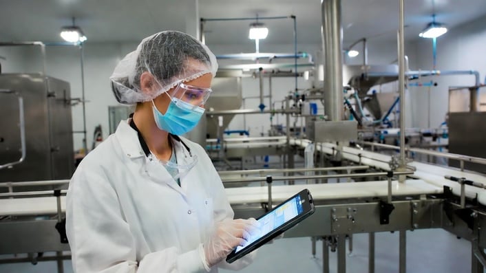 Food scientist using a tablet while inspecting production line equipment in a modern food processing facility.