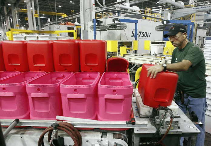 Factory worker in a green shirt handling red plastic cooler components on a manufacturing production line.