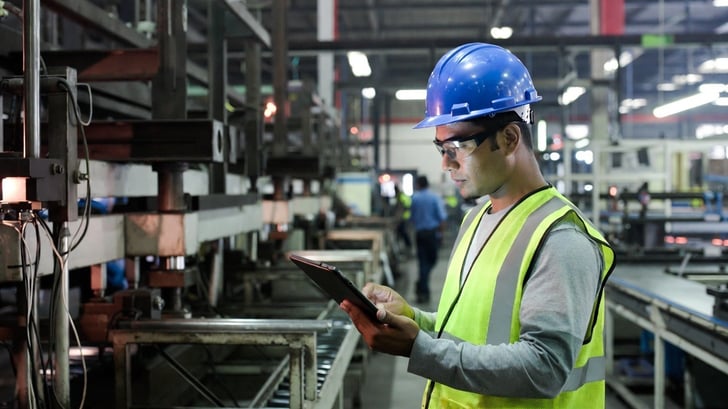 Manufacturing worker using a tablet on the shop floor to manage production scheduling.