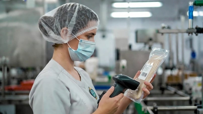 A quality control worker in a food manufacturing facility scanning a product packaging using a mobile device.