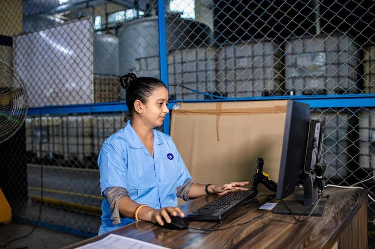 Manufacturing worker reviewing production schedule and inventory data on a computer screen in a factory setting.