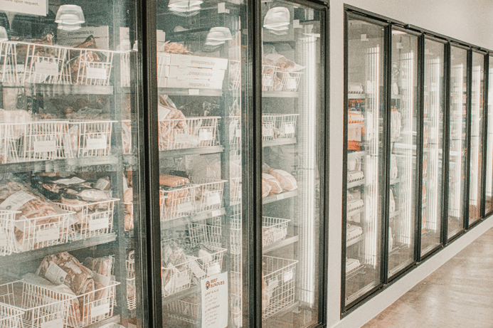 Glass-door commercial freezers stocked with packaged meats and frozen goods in a store.