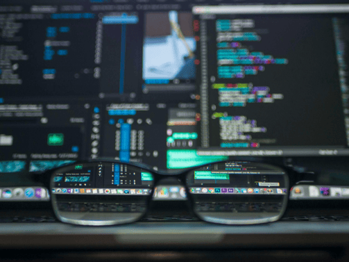 Eyeglasses resting in front of a computer screen displaying colorful code and developer tools.