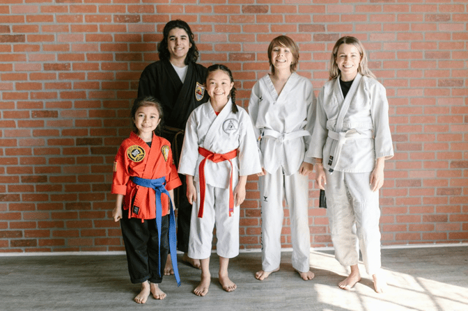 Group of children and teens in martial arts uniforms posing together at a karate training studio.