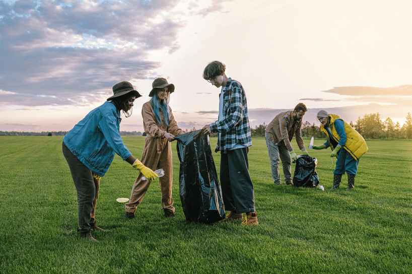 A Group of five volunteers picking up litter with garbage bags in a grassy field at sunset.