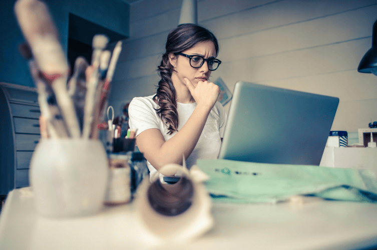 Woman with glasses and braided hair looking thoughtfully at laptop screen.