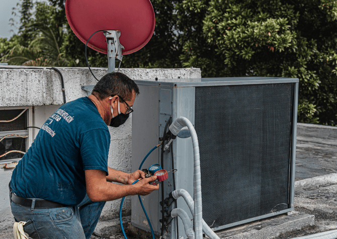 HVAC technician servicing an outdoor AC unit on a rooftop.