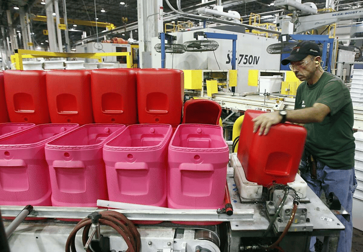 Factory worker handling red plastic containers on a production line in a manufacturing facility.
