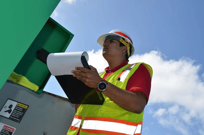 Inspector in a hard hat and high-visibility vest holding a clipboard.