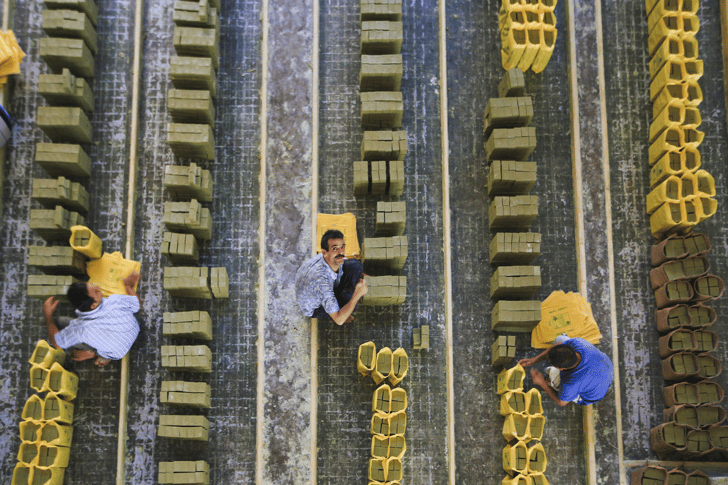 Overhead view of workers carrying and stacking blocks of soap in rows at a factory.