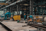 Workers in blue uniforms cutting and grinding metal inside a large industrial steel fabrication workshop.