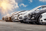 Row of modern parked cars in a dealership or rental lot under a partly cloudy sky, representing fleet management for car rental businesses.