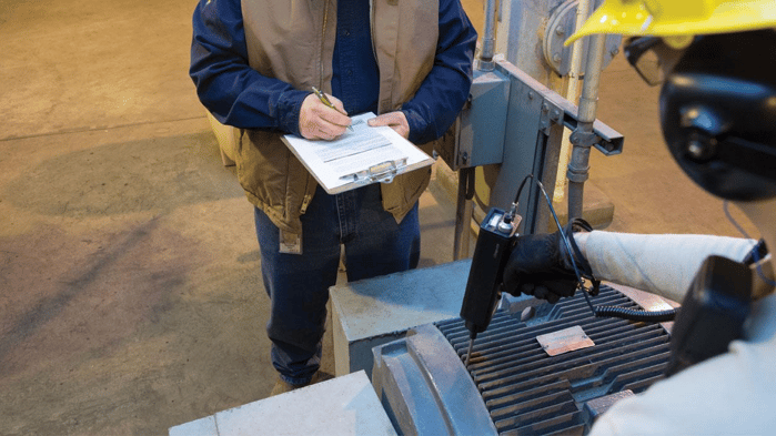 Factory personnel taking notes while inspecting a machine