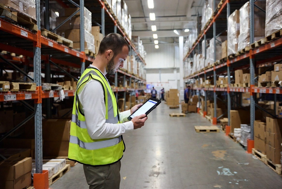 A supply chain worker using a mobile app on a tablet to carry out an inspection on a warehouse floor