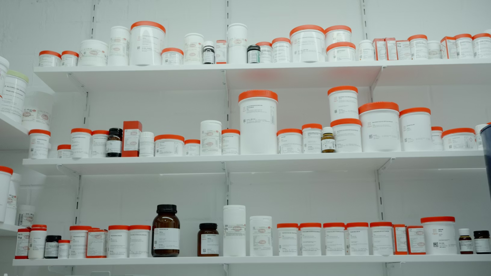 A shelf with lots of white and orange medication bottles