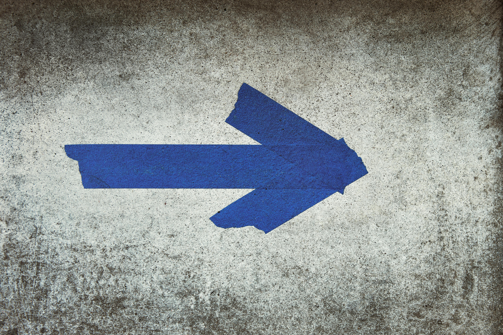 Blue arrow painted on a weathered concrete surface pointing to the right.