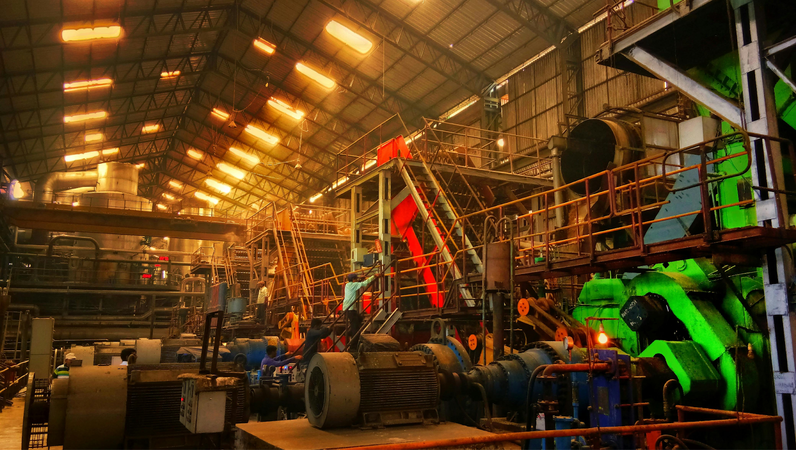 Industrial factory interior with large machinery, metal walkways, overhead lighting, and complex equipment in an orange ambiance.