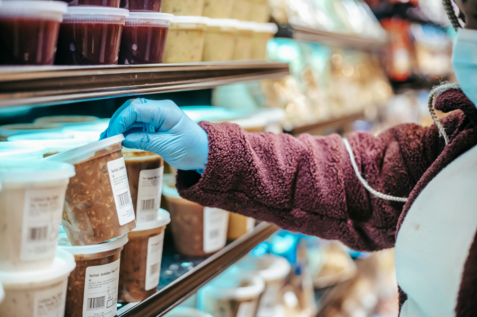 Hand in blue glove selecting food item from refrigerated display case in food service setting.