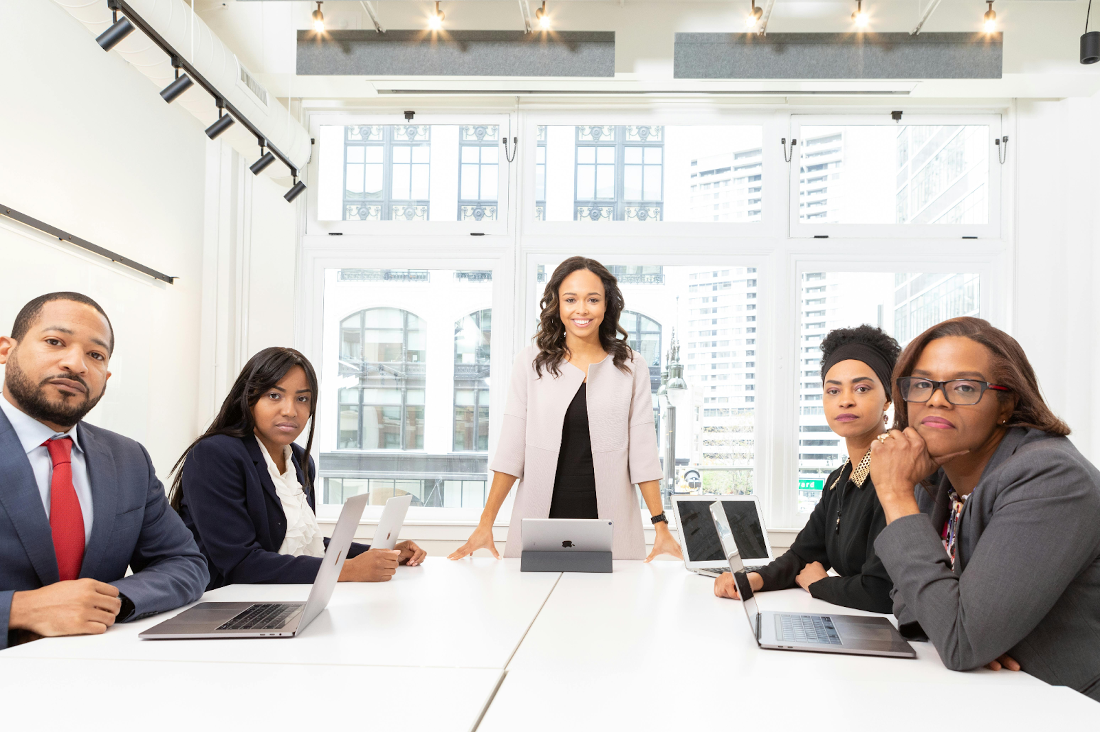 Woman leads business meeting with four colleagues around a conference table in a modern city office.