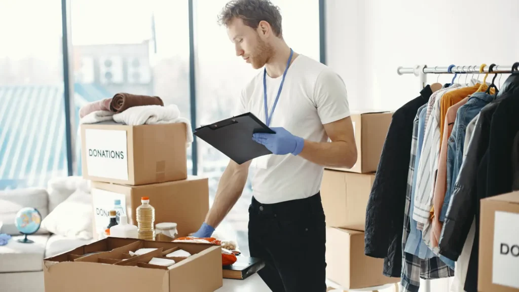 Male volunteer with clipboard and gloves sorting donated clothing and supplies into cardboard boxes. (Image courtesy of Peak Outsourcing)